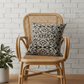Wicker chair with a handprinted linen cushion against a white brick wall