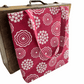 Pink tote bag with white floral pattern draped over a wooden suitcase.